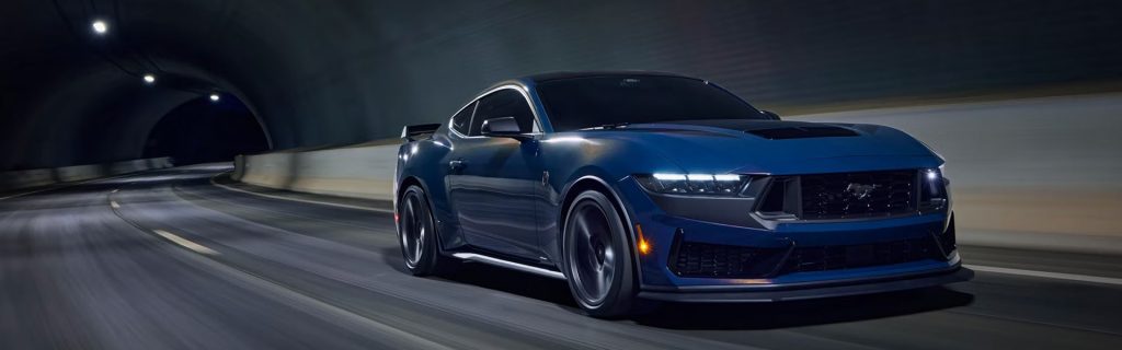 The image showcases a blue Ford Mustang speeding through a tunnel, highlighting its aggressive, sleek design with dynamic motion, perfect for high-performance driving.
